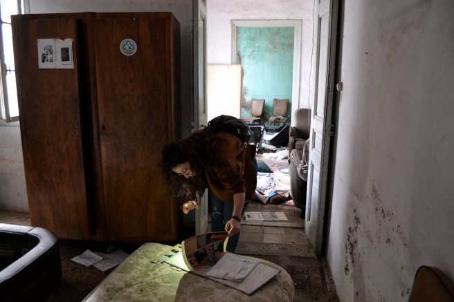 Mezher uses the torch on her phone to look through an old scrapbook full of cut-out photographs from vintage magazines